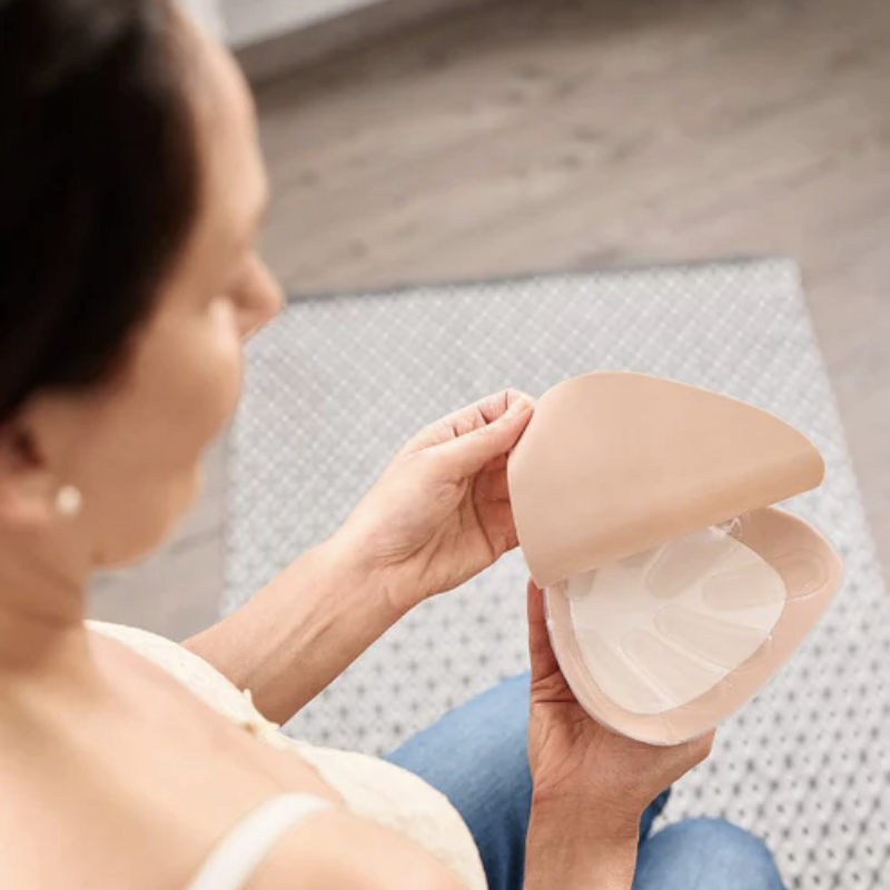 Woman holding an Amoena Contact Comfort+ breast form, showing the adhesive side designed for secure attachment after mastectomy.