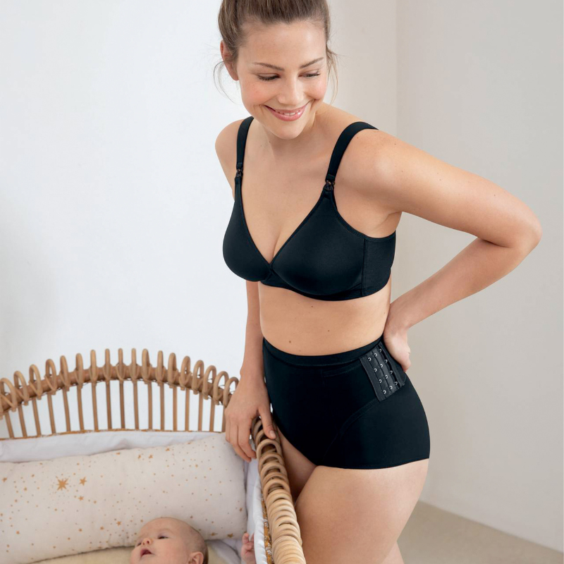 Woman post partum next to crib with baby wearing the Anita spacer nursing bra and Anita rebelt brief